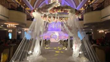 An indoor venue with a central aisle leading to a stage, surrounded by balconies and chandeliers.