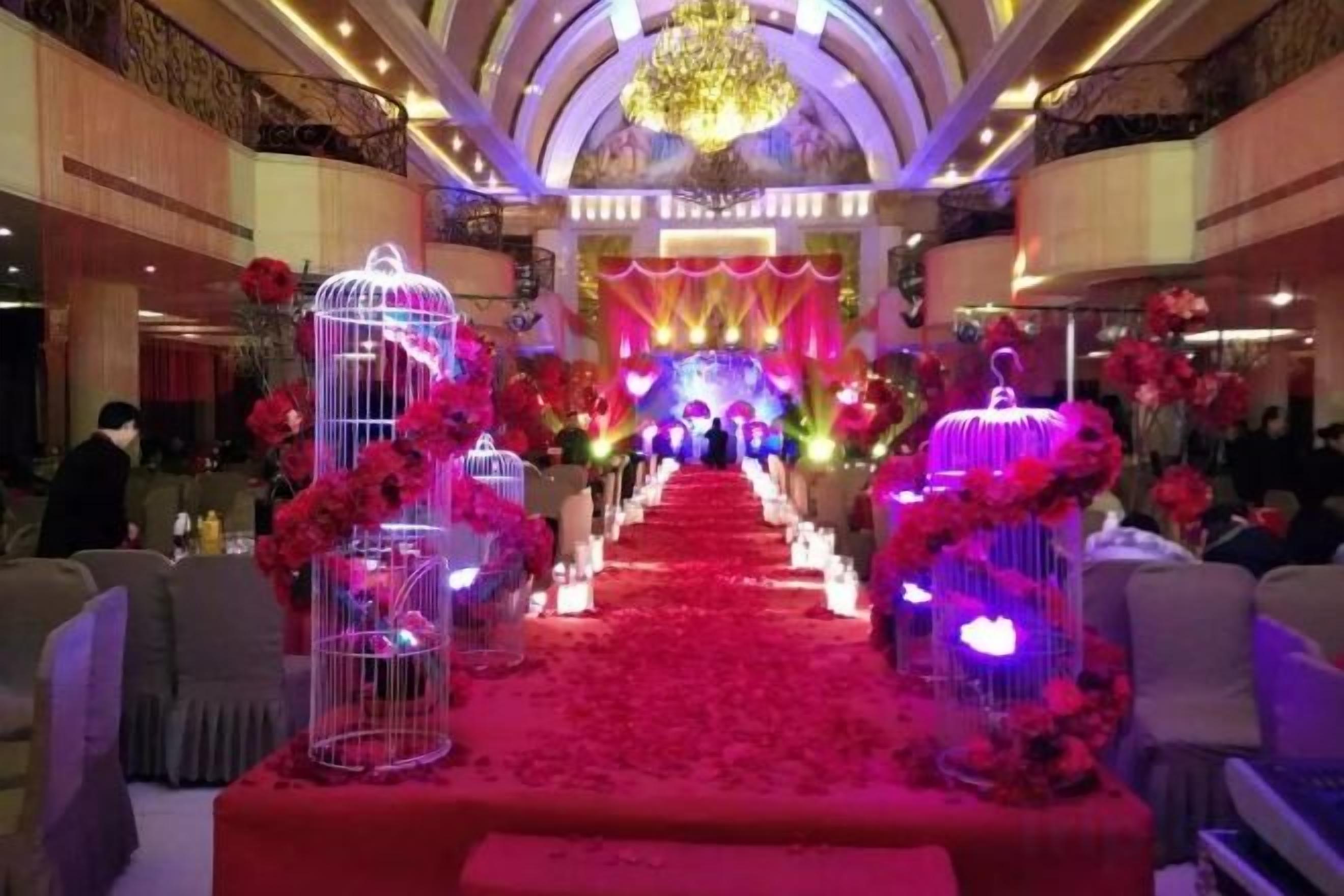 A banquet hall with a red carpet aisle, floral decorations, and a chandelier.