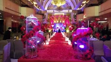 A banquet hall with a red carpet aisle, floral decorations, and a chandelier.