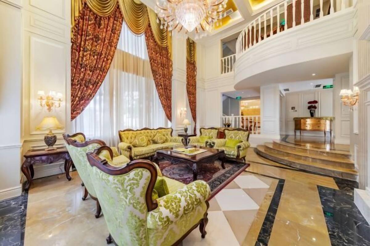 A grand lobby with ornate furniture, a chandelier, and a checkered floor.