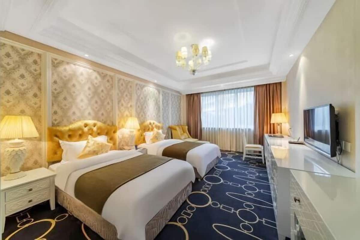 A hotel room with two beds, a television, a desk, and a chandelier.