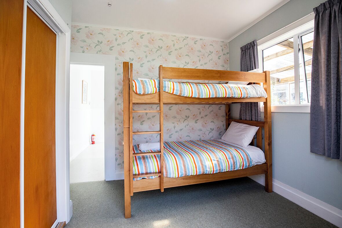 A bunk bed with a ladder, a window with curtains, and floral wallpaper.