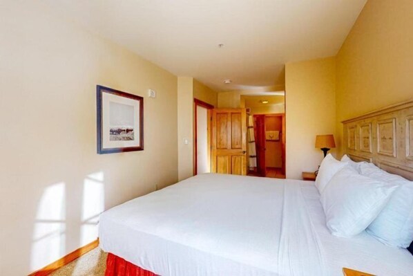 A hotel room with a large bed, a framed picture on the wall, and a wooden door leading to a hallway.
