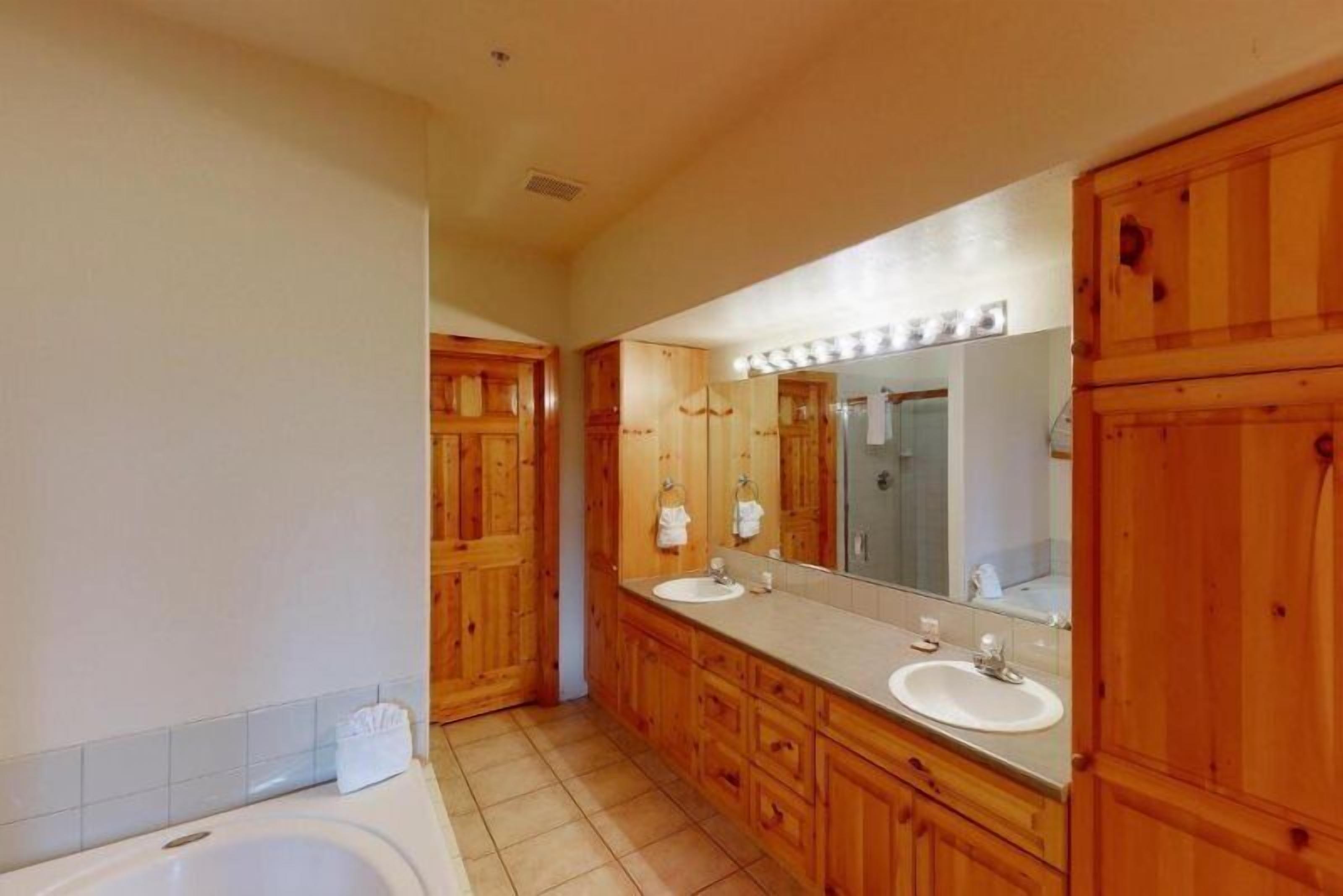 A bathroom with wooden cabinets, a large mirror, a bathtub, and a vanity with a sink.