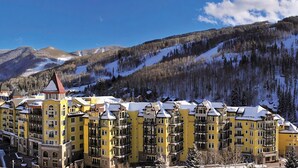 A multi-story hotel with a yellow facade, located in a mountainous area with snow-covered slopes. - The Ritz-Carlton Club®, Vail, Colorado. 2 Bedroom + DEN. 8PAX (Vail)
