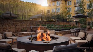A circular outdoor seating area with a fire pit, surrounded by wicker chairs and a stone wall. - The Ritz-Carlton Club®, Vail, Colorado. 2 Bedroom + DEN. 8PAX (Vail)