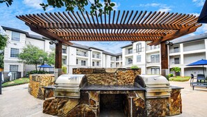 An outdoor barbecue area with stone walls and a wooden pergola. - Mid-rise Haven in the Heart of Downtown And Midtown (Houston)