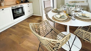 A modern kitchen with white cabinets, a built-in oven, and a dining area with wicker chairs and a round table set for six. - Secretapartment: Zentral und Gemütlich, mit Großem Balkon (Warburg)