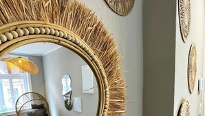A room with a large mirror surrounded by woven decorative elements, a wicker chair, and wall art. - Secretapartment: Zentral und Gemütlich, mit Großem Balkon (Warburg)