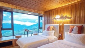 Une chambre avec deux lits, un plafond en bois, une grande fenêtre donnant sur la montagne et une table avec une chaise.