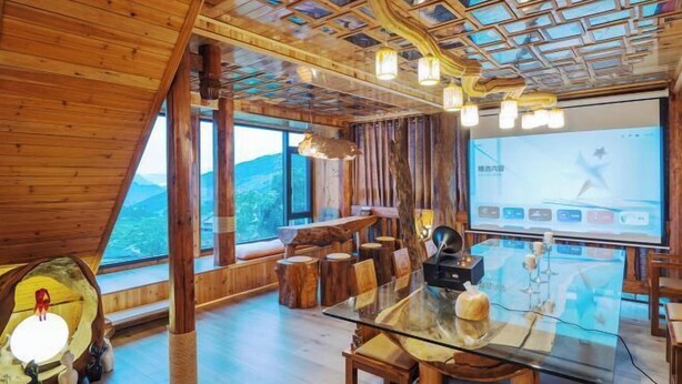 Un intérieur en bois avec une table en verre, des chaises en bois, un écran de projection et une vue sur l’extérieur.