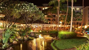 A well-lit outdoor area with a pool, palm trees, and a building with multiple floors and balconies. - Ocean View-1Bdrm:1Bath -Westin Kaanapali Maui North Villas (Lahaina)