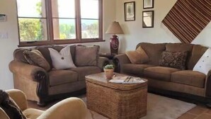 A living room with two sofas, a coffee table, and a lamp. There is a large window providing natural light. - Peaceful spacious Spanish style Casita in Wine Country (Santa Ynez)