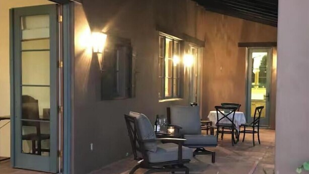 A covered patio area with a table and chairs, a small table with a candle, and a door leading to an interior space. - Peaceful spacious Spanish style Casita in Wine Country (Santa Ynez)