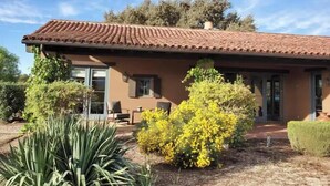 A two-story house with a tiled roof, a patio with outdoor furniture, and a garden with yellow flowering plants. - Peaceful spacious Spanish style Casita in Wine Country (Santa Ynez)
