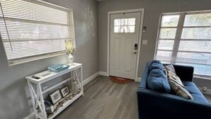 A living room with a blue sofa, a white console table with decorative items, and a door with a window.