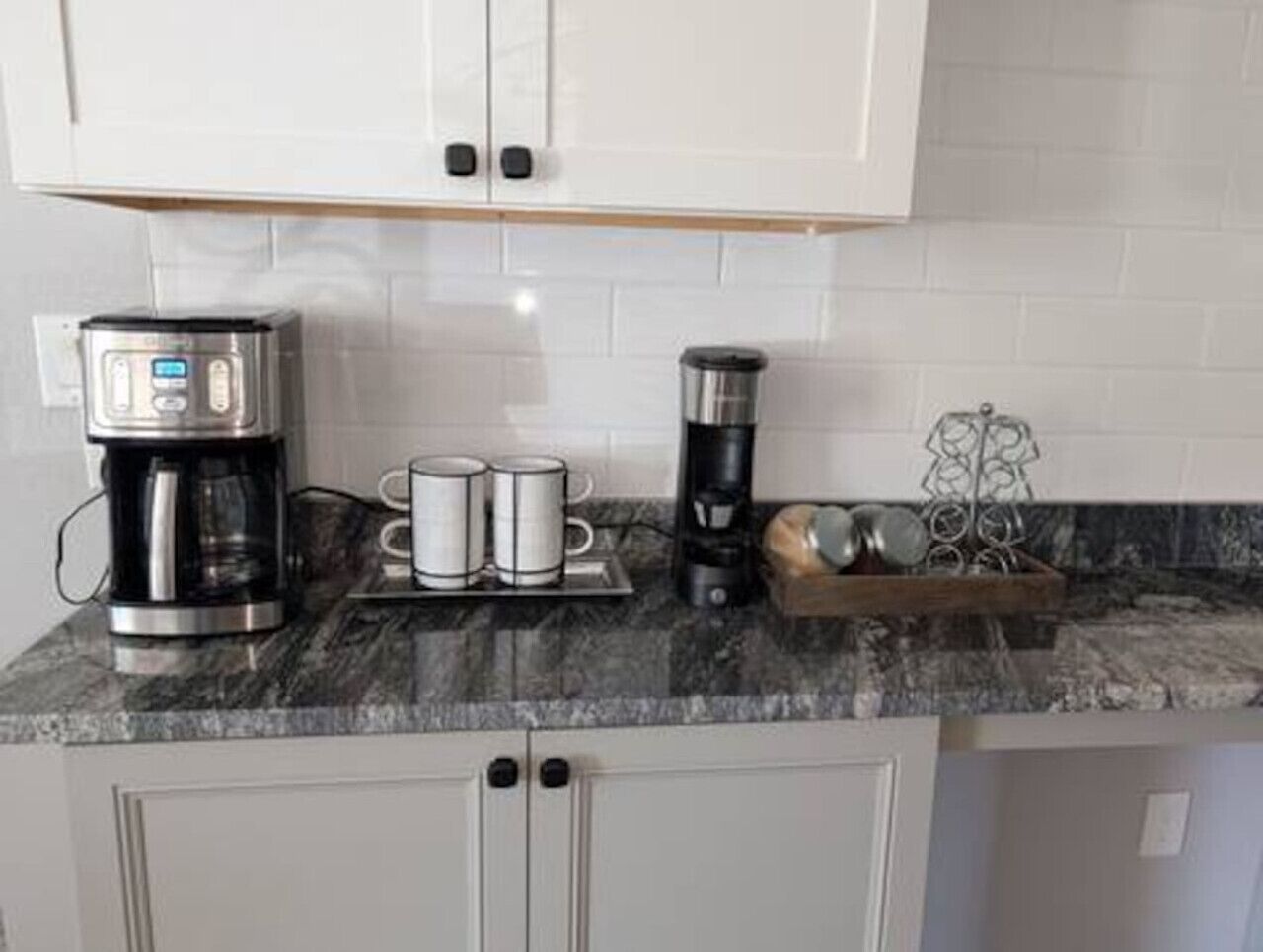 A kitchen with a coffee maker, two mugs, a kettle, and a metal rack with utensils.