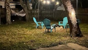 A backyard with a hammock, two blue chairs, and a fire pit.