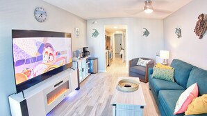 Una sala de estar moderna con un televisor de pantalla plana, una cafetera, un sofá y un comedor.