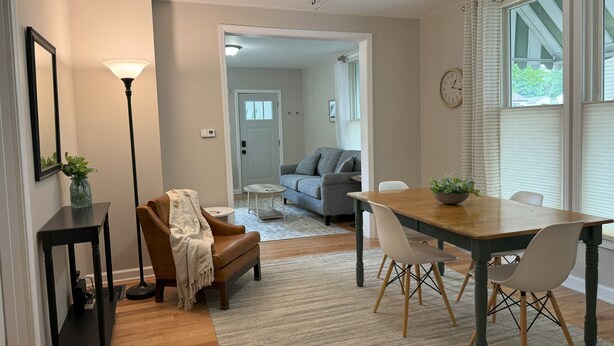 Un coin repas avec une table et des chaises en bois, une petite table d’appoint avec un vase, et un canapé à l’arrière-plan.