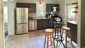 Une cuisine moderne équipée d’un réfrigérateur en acier inoxydable, d’un four à micro-ondes et d’une cuisinière à gaz. On y trouve deux tabourets en bois et une petite table ronde.