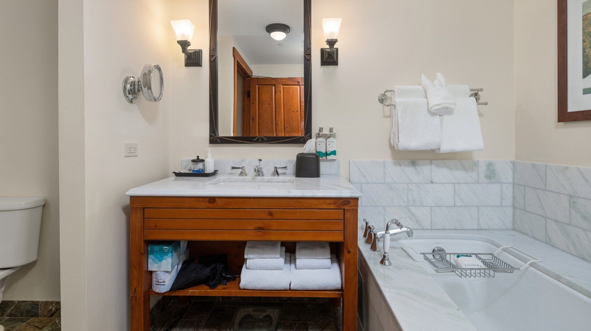 A bathroom with a wooden vanity, a large mirror, a sink with a soap dispenser, and a bathtub.