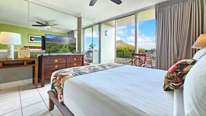 A hotel room with a bed, a desk, a television, and a balcony with a view of the mountains.
