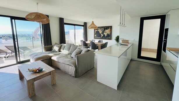A modern living room with a sofa, a dining table, and a kitchen area.
