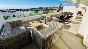 A rooftop terrace with wicker furniture, a table, and a view of the cityscape.
