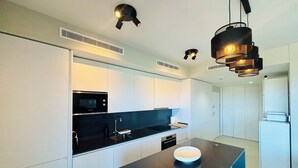 Een moderne keuken met witte kasten, een zwart aanrecht, een Bosch magnetron en een zwarte hanglamp.