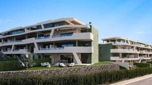 Een modern meerlaags hotel met balkons, een zwembad en een verzorgde tuin.