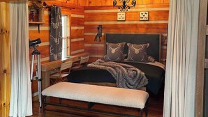 A log cabin bedroom with a bed, bench, director's chair, and a tripod.