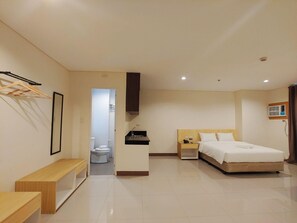 Ein modernes Hotelzimmer mit Bett, Nachttisch und kleinem Schreibtisch mit Stuhl. Ein Badezimmer ist durch eine geöffnete Tür sichtbar.