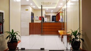 A reception area with a wooden desk, a glass partition, and two potted plants. - Reddoorz Plus @ Kaizen Suites Taft Avenue (Manila)