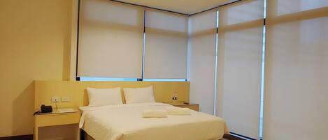 A modern bedroom with a large bed, bedside tables, and a window with blinds.