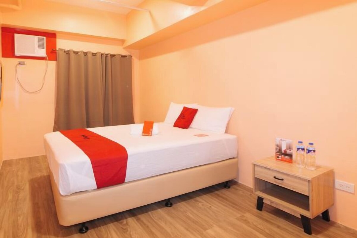 A hotel room with a bed, a nightstand, a wall-mounted air conditioner, and a curtain.