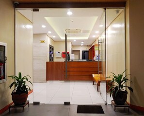 A reception area with a wooden desk, a glass partition, and two potted plants. - Reddoorz Plus @ Kaizen Suites Taft Avenue (Manila)