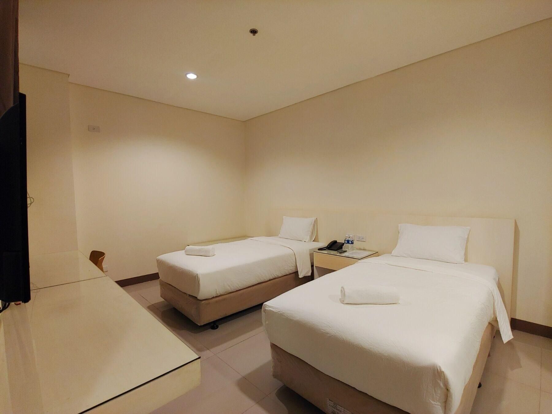 A hotel room with two beds, a desk, and a television.