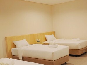 A hotel room with two beds, each with white linens and pillows. There is a wooden headboard on the left bed, and a small table with a bottle and a glass on the right bed. - Reddoorz Plus @ Kaizen Suites Taft Avenue (Manila)