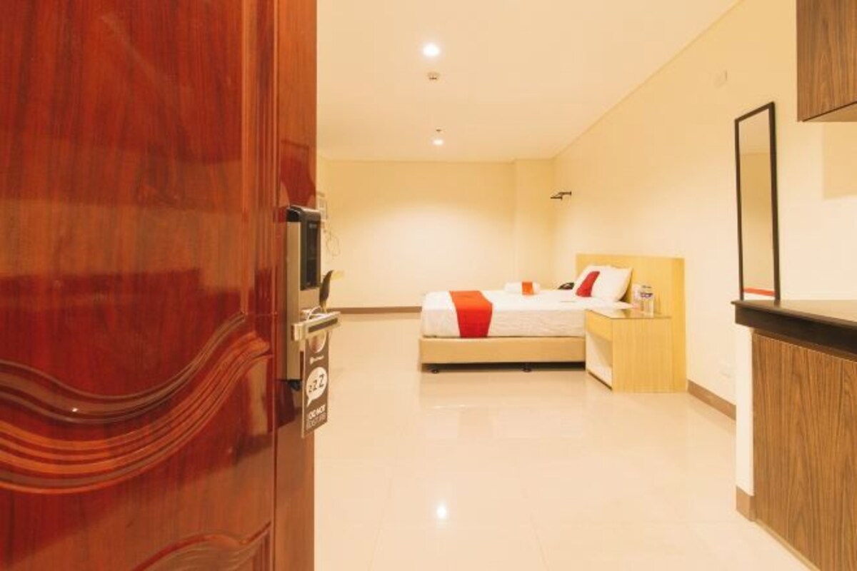 Une chambre d’hôtel avec un lit, une table de chevet, un bureau en bois et un miroir au mur.