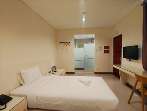 Habitación de hotel con una cama, un escritorio, un televisor y un baño visible a través de una puerta abierta.
