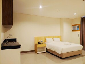 A hotel room with a bed, a nightstand, a small desk with a phone, a sink, and an air conditioning unit. - Reddoorz Plus @ Kaizen Suites Taft Avenue (Manila)