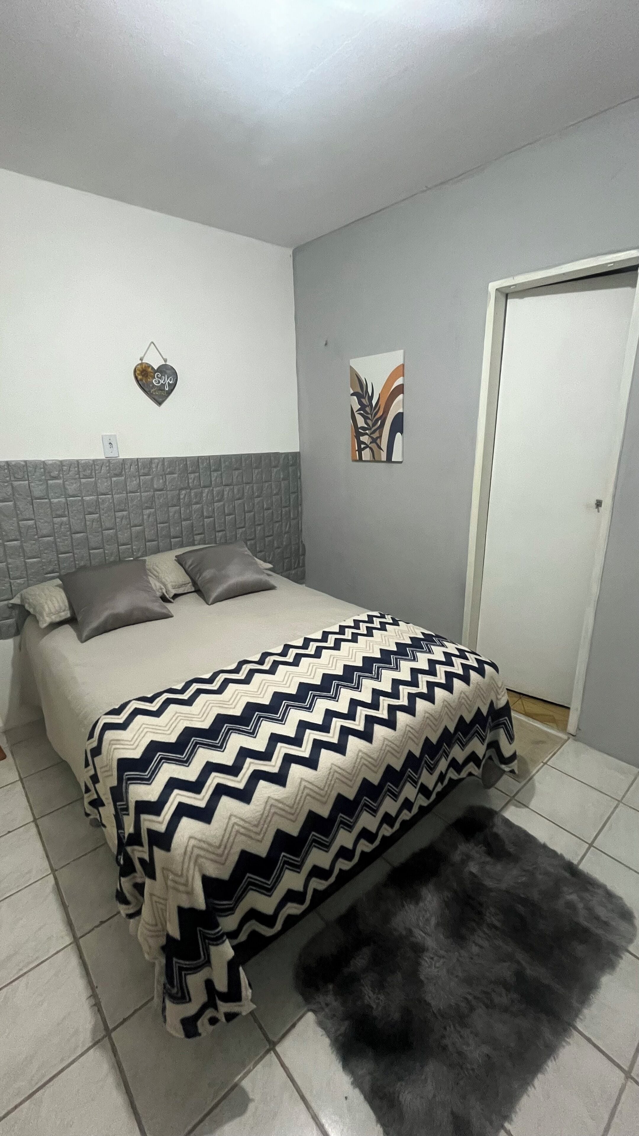 A bedroom with a bed, grey headboard, grey walls, a door, and a rug.