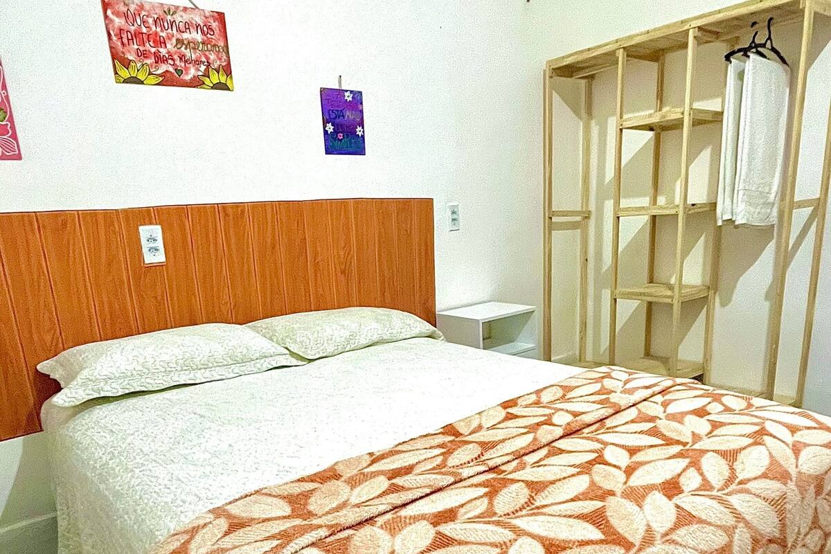 A bedroom with a bed, a wooden headboard, a hanging towel rack, and two wall decorations.