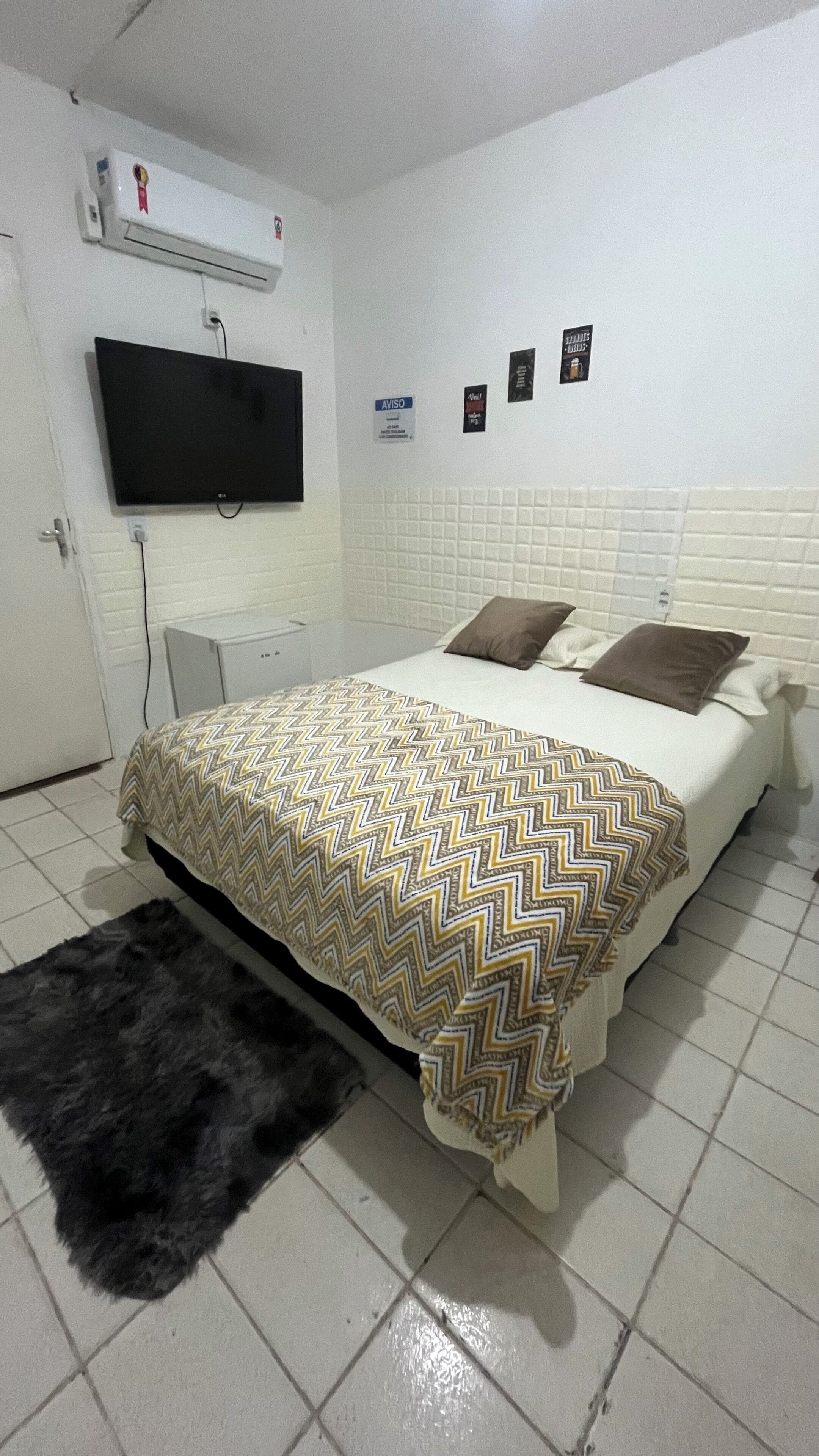 Habitación de hotel con cama, televisor montado en la pared, escritorio pequeño y alfombra negra.