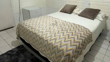 Een hotelkamer met een bed, een aan de muur bevestigde televisie, een klein bureau en een zwart tapijt.