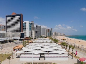 A coastal cityscape with modern high-rise buildings, a beach, and a covered pedestrian area with white canopies. - Pousada Mar e Sol (Fortaleza)