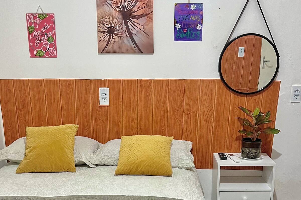 A neatly arranged bedroom with a bed, a bedside table with a plant, and a wall-mounted mirror.