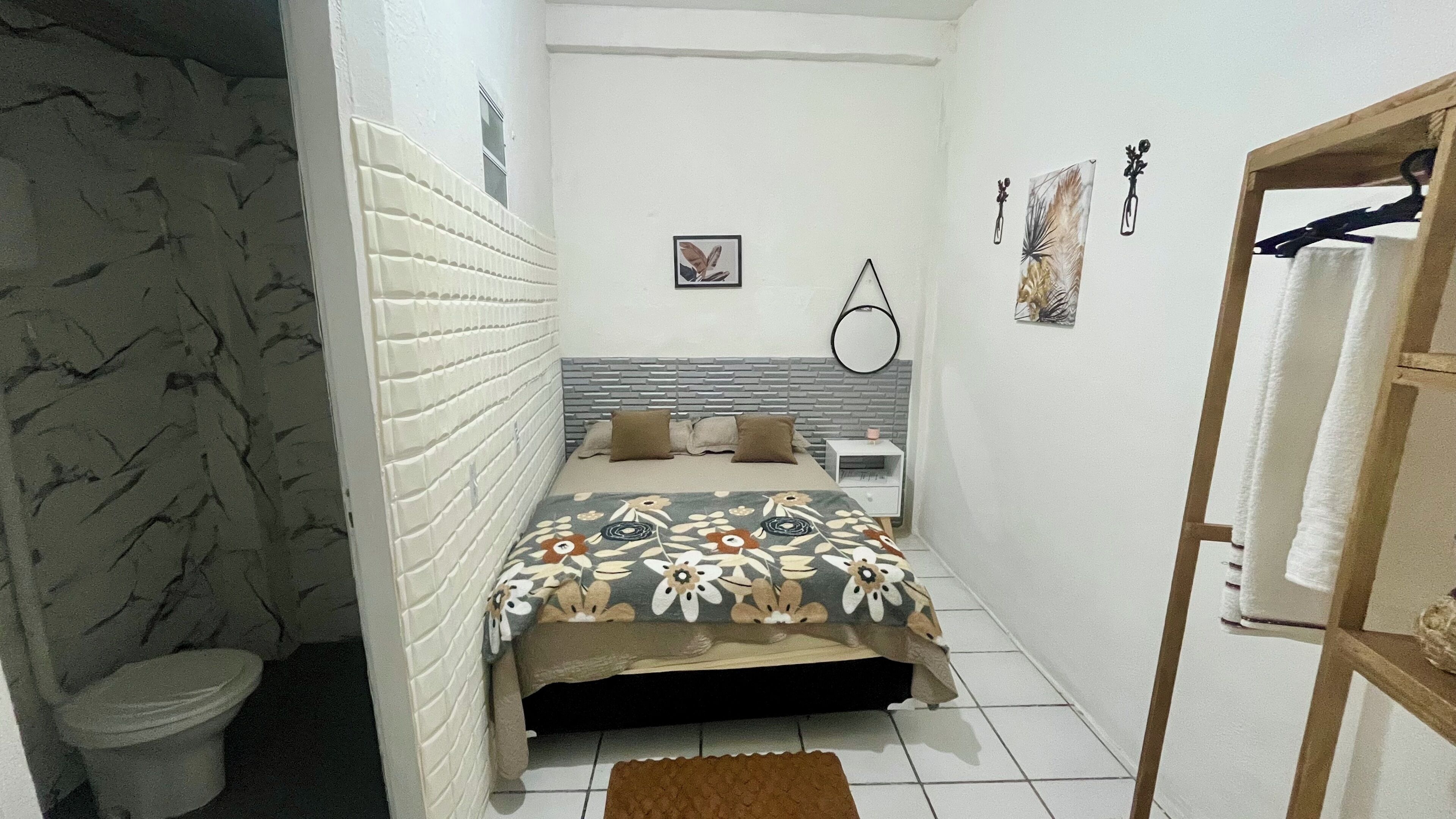 Ein kleines, gemütliches Schlafzimmer mit Bett, Nachttisch, Spiegel und einem Händetuchhalter an der Wand.