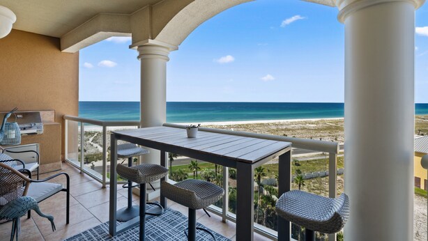 A balcony with a table and chairs, overlooking a beach and ocean.